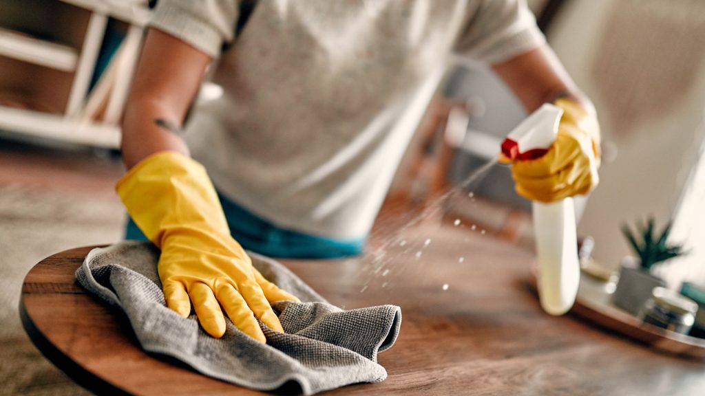 Person cleaning a table with spray and cloth.