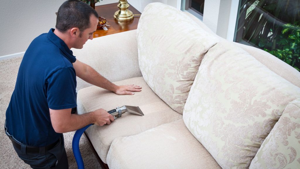 Man cleaning beige sofa upholstery.